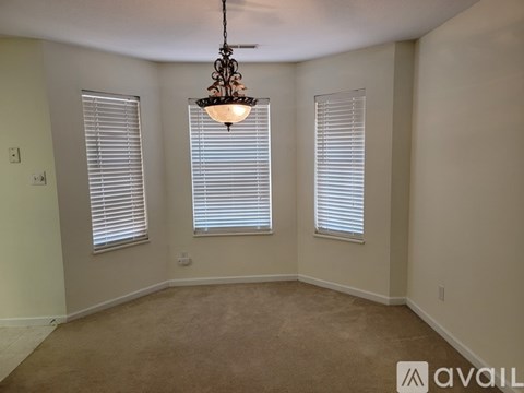 A room with a chandelier, two windows with blinds, and a carpeted floor.