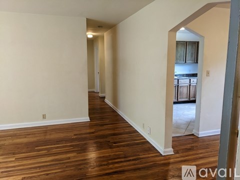 A room with wooden floors and white walls, leading to a kitchen area.