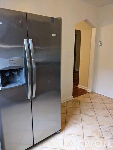 A stainless steel refrigerator in a kitchen with a white wall and tile floor.