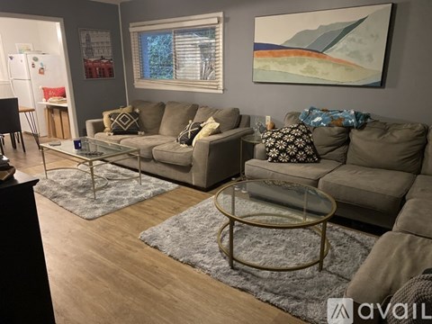 A living room with a grey couch, a glass coffee table, and a painting on the wall.
