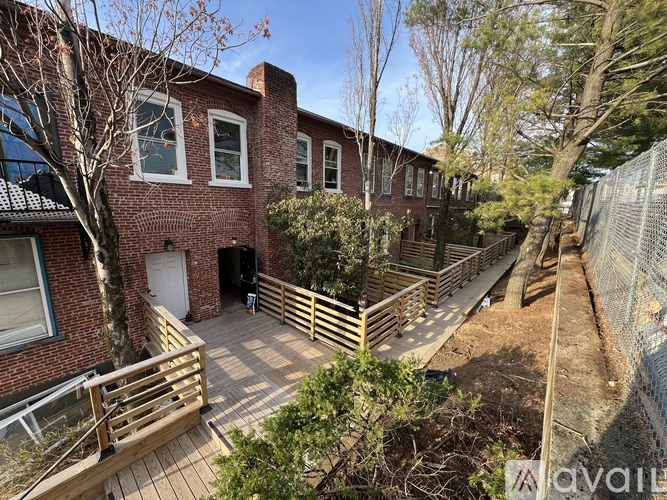A brick building with a white door and windows, surrounded by a wooden fence and trees.