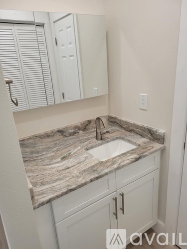A bathroom with a marble countertop and white cabinets.