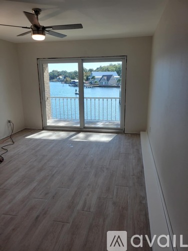 A room with a sliding glass door leading to a balcony with a view of a lake and houses.
