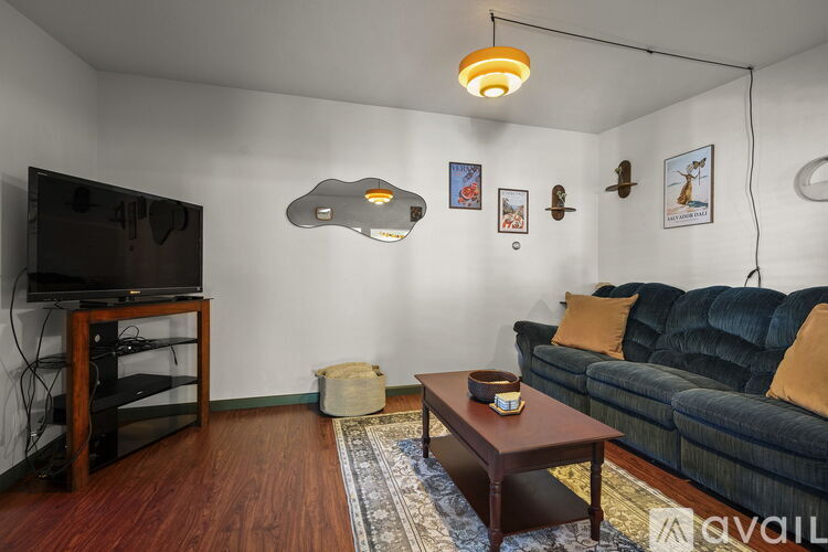 A living room with a black couch, a wooden coffee table, a flat screen TV on a wooden stand, and a rug on the floor.