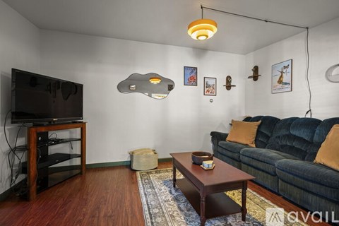 A living room with a black couch, a wooden coffee table, a flat screen TV on a wooden stand, and a rug on the floor.