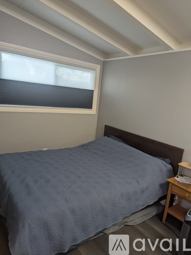 A bedroom with a bed, nightstand, and window with blinds.