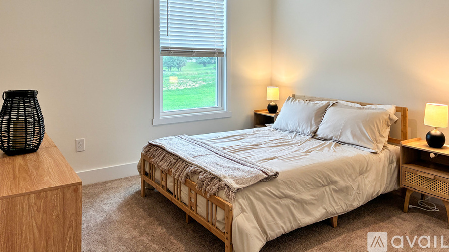 A bedroom with a large bed and a window overlooking a green lawn.