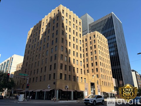 A tall building with many windows is in the foreground of a city street.