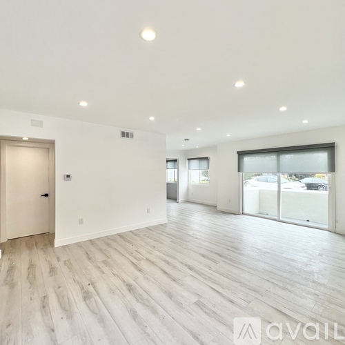 A spacious room with wooden flooring and large windows.