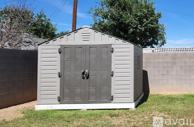 A gray outhouse with a door in the middle is situated in a grassy area.