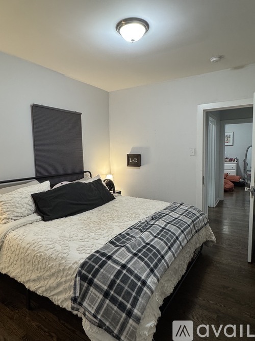 A bedroom with a bed, a window with blinds, and a lamp on the wall.