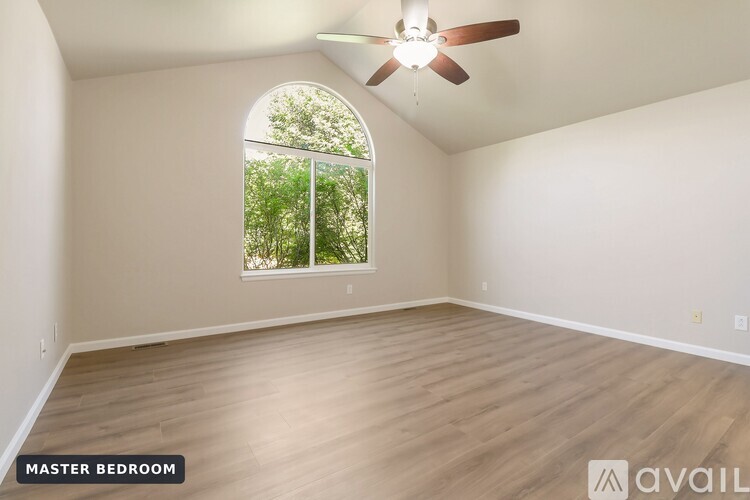A spacious master bedroom with a large window and hardwood flooring.