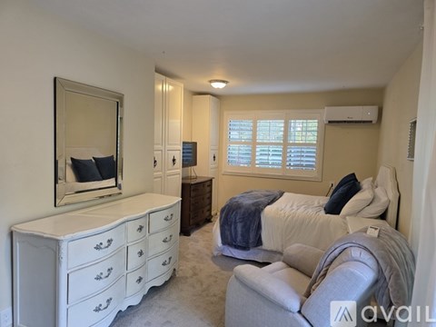 A bedroom with a white dresser and a bed with a blue blanket.
