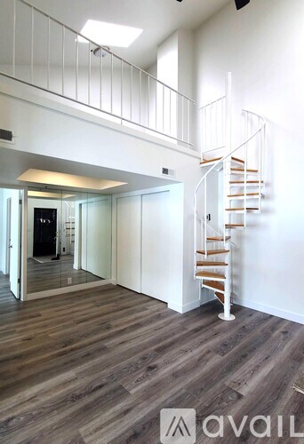 A spacious room with a wooden floor and a white staircase.