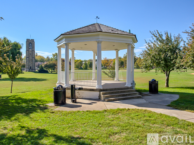 A gazebo is surrounded by a grassy area and a clock tower is in the background.