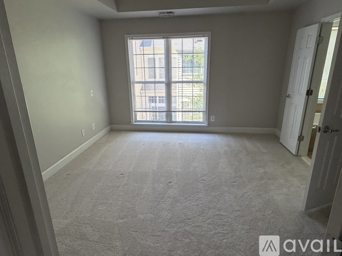 A room with a carpeted floor and a large window with blinds.