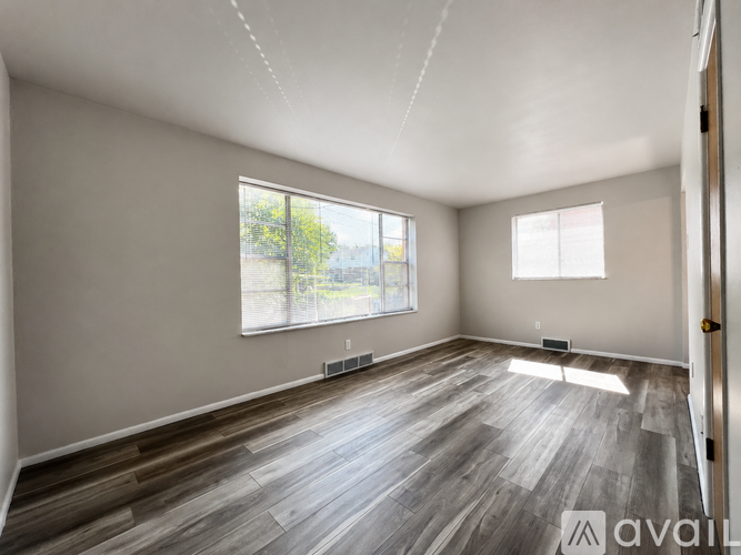 A spacious room with wooden flooring and two windows.