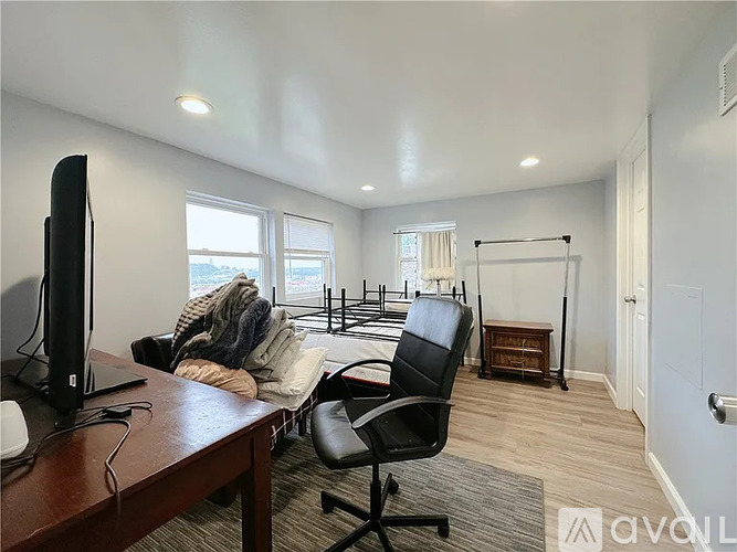 A room with a black chair, a television, and a window with a view of a building outside.