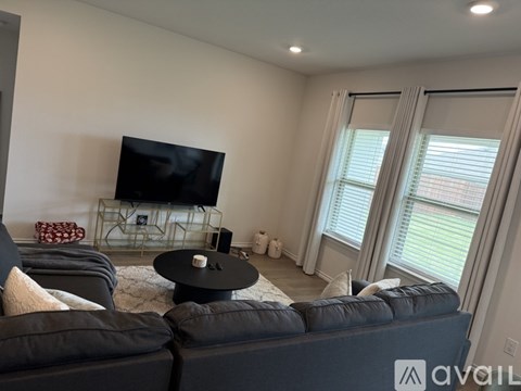 A black leather couch in a living room with a flat screen TV on a stand.