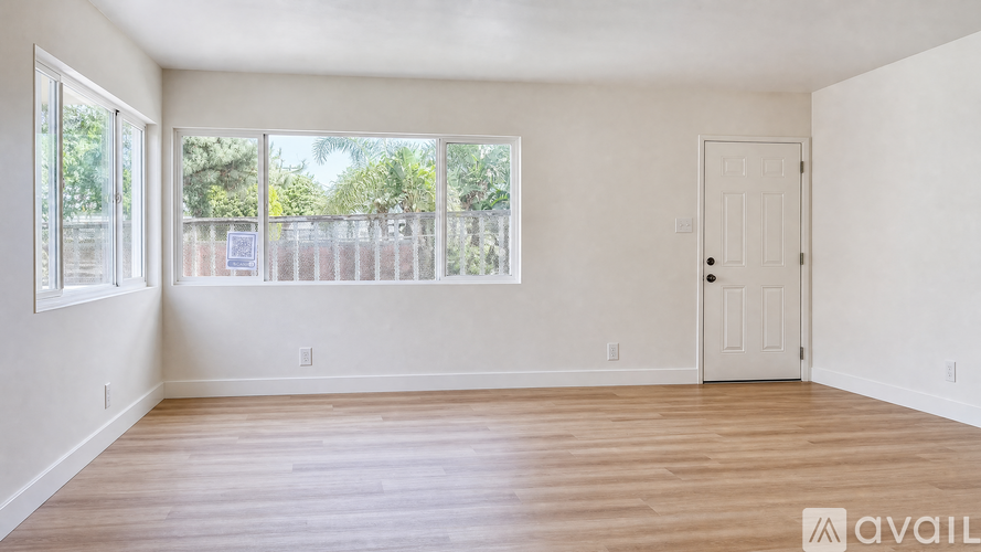 A room with a door and a window with a view of a fence and trees.