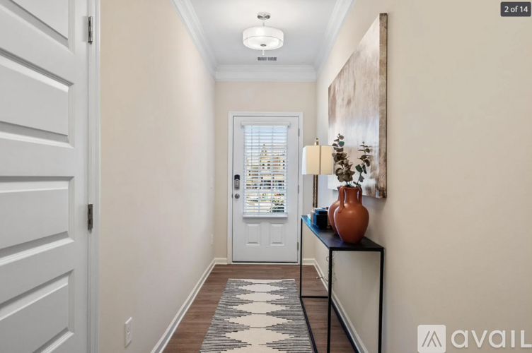 A hallway with a white door, a vase on a table, and a painting on the wall.