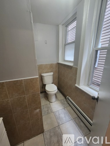 A bathroom with a toilet, tiled walls, and a window.