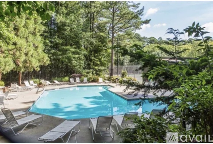 A pool surrounded by trees and lounge chairs.