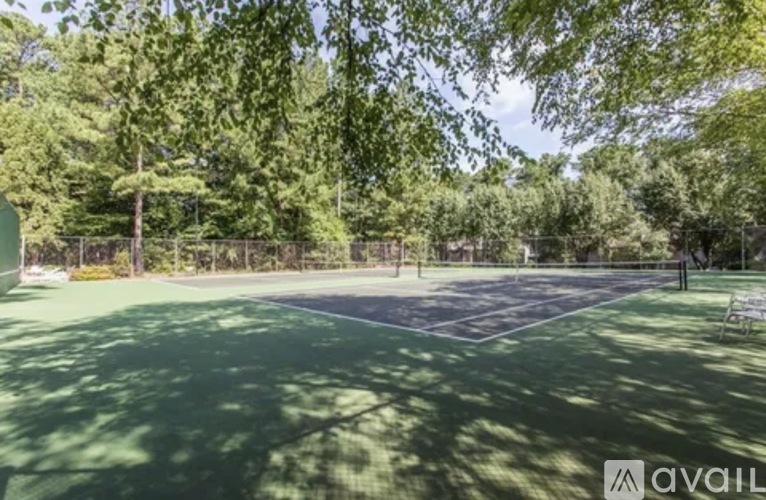 Tennis court surrounded by trees and a fence.