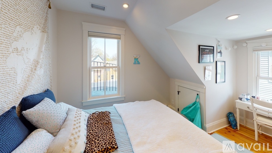 A bedroom with a bed, a desk, and a window with a view of a fence and trees.