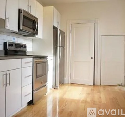 A kitchen with white cabinets and appliances, a door and a wall.