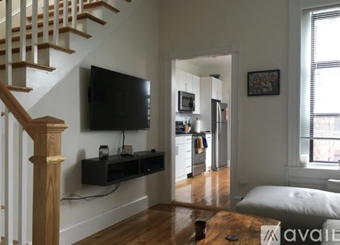 A living room with a staircase on the left and a television on the wall.
