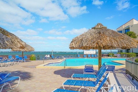 A pool area with blue lounge chairs and thatched umbrellas.