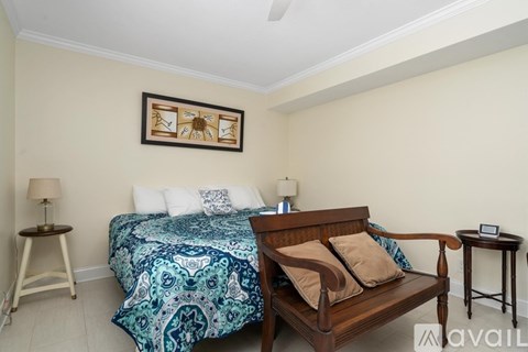 A bedroom with a bed, a bench, and a table with a lamp on it.