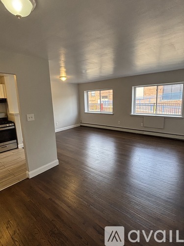 A room with wooden floors and a window with a view of a fence and a building.