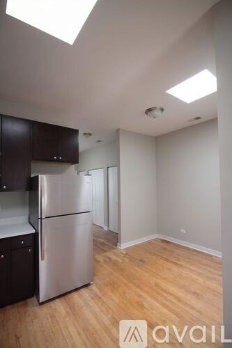 A kitchen with a refrigerator, cabinets, and a wooden floor.