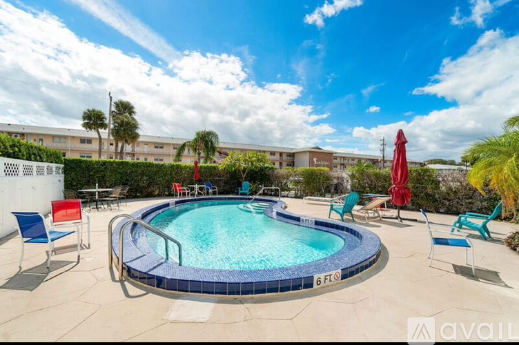 A pool surrounded by chairs and umbrellas with a building in the background.