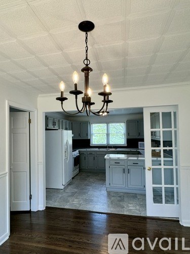 A chandelier hangs over a kitchen island with a sink and a window.