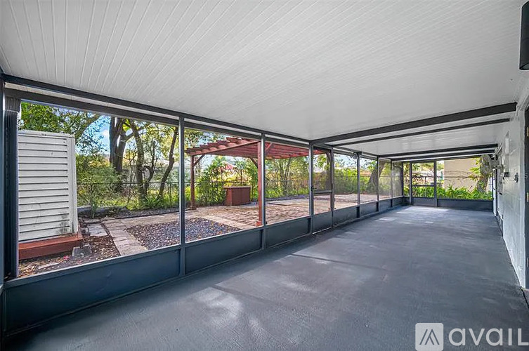 A covered outdoor area with a view of a garden and trees.
