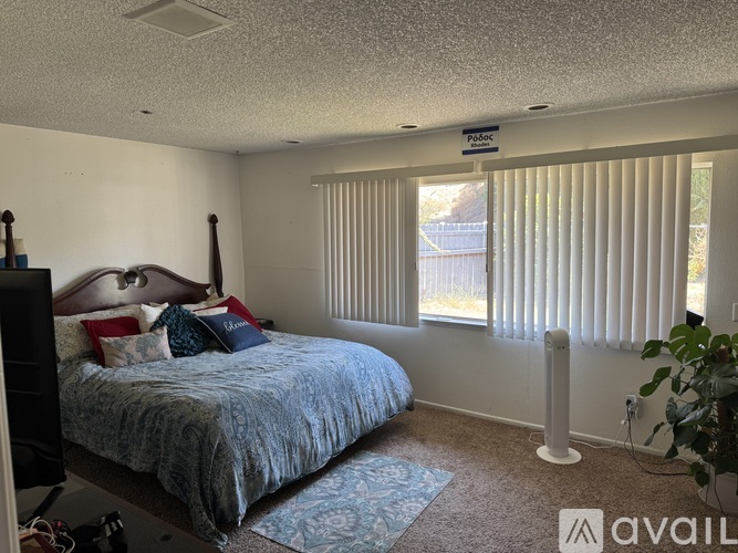 A bedroom with a bed, pillows, and a window with blinds.