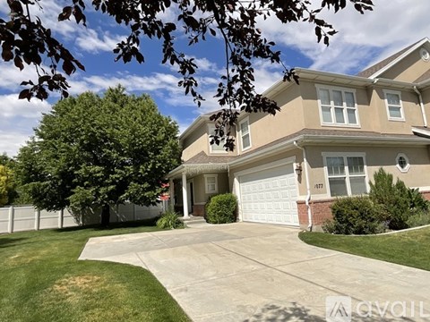 A house with a white garage door is surrounded by a white fence and has a tree in front of it.