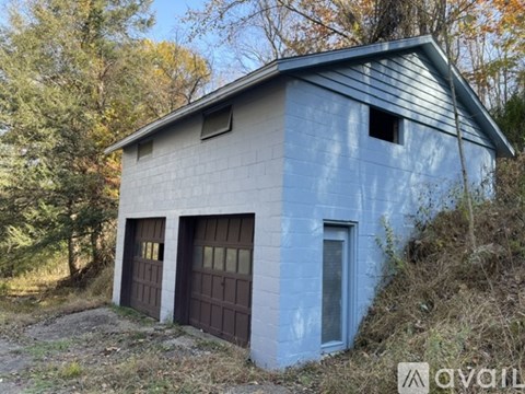 A small blue building with a brown door sits in a wooded area.
