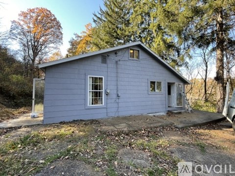 A small blue house with a porch and a tree in the background.