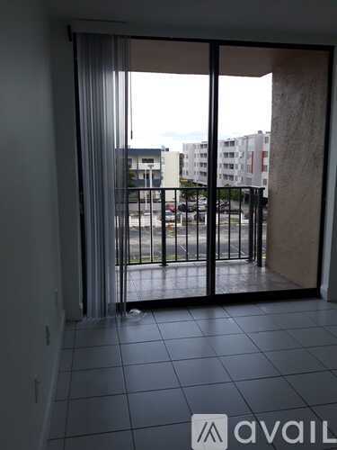 A balcony with a black railing and a view of a parking lot and buildings.