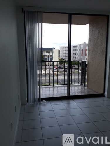 A balcony with a black railing and a view of a parking lot and buildings.