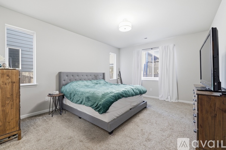 A bedroom with a bed, a television, and a window with white curtains.