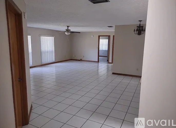 A spacious room with white tiled flooring and a ceiling fan.