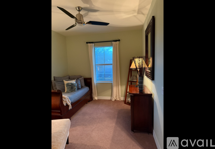 A bedroom with a bed, a window with curtains, a ceiling fan, and a nightstand with a lamp.