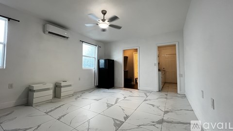 A spacious room with a black refrigerator and a ceiling fan.