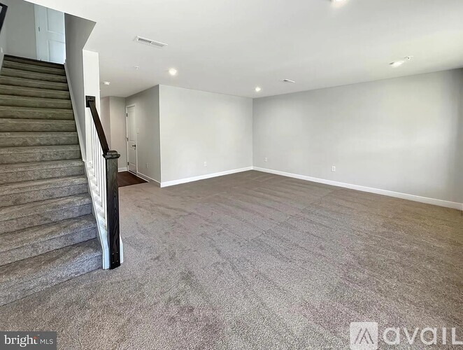 A spacious room with a staircase on the left side and carpeted flooring.