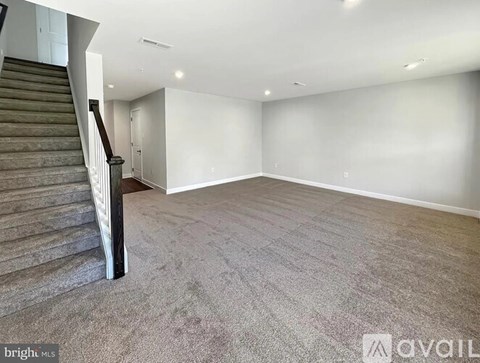 A spacious room with a staircase on the left side and carpeted flooring.